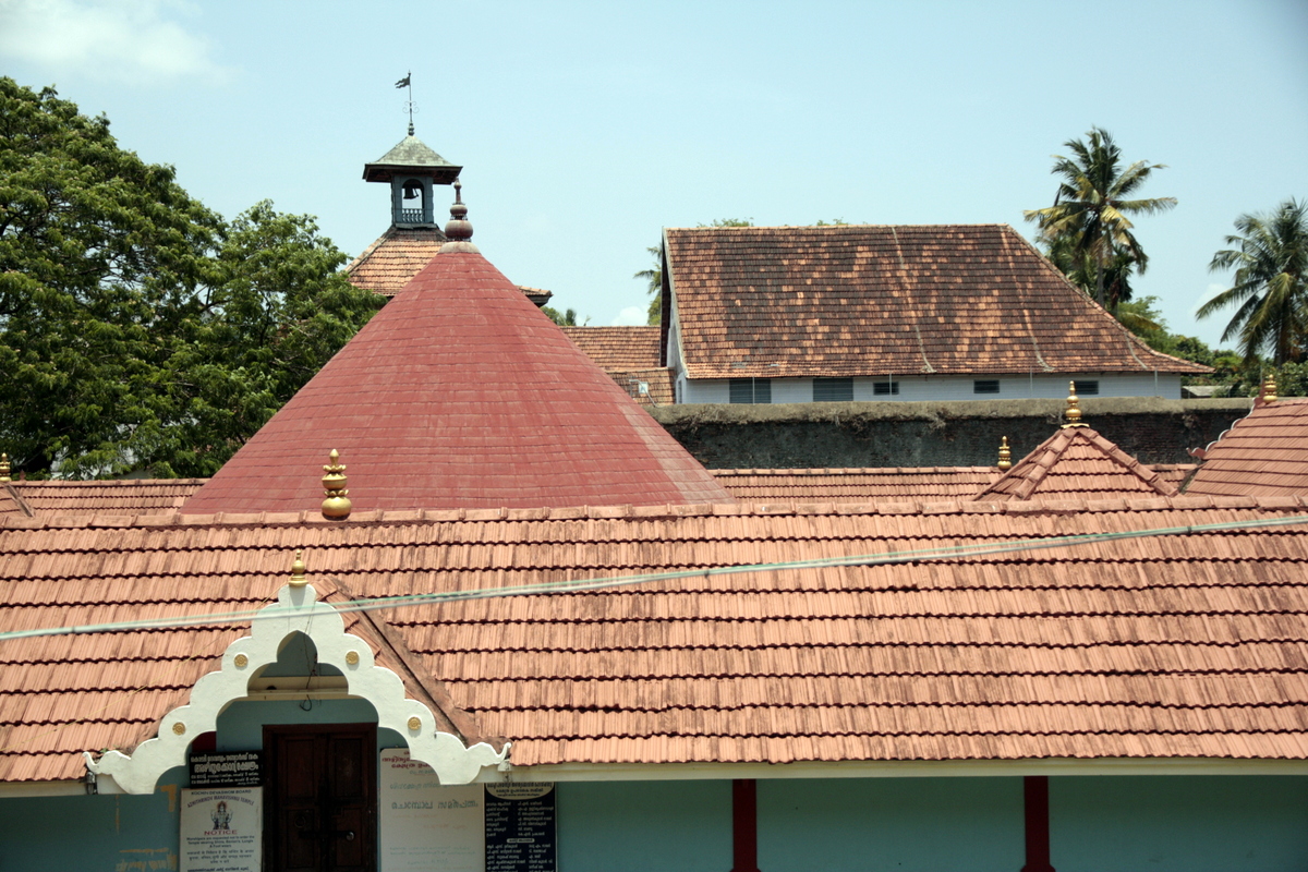 In the foreground is the entry door and roof of the temple inside the Mattancherry Palace. The central circular roof of the temple is made of copper plates. Beyond the compound wall in the middle is the Jewish Synagogue. Both are made with terracotta tiles, a traditional roofing material in Kerala.  